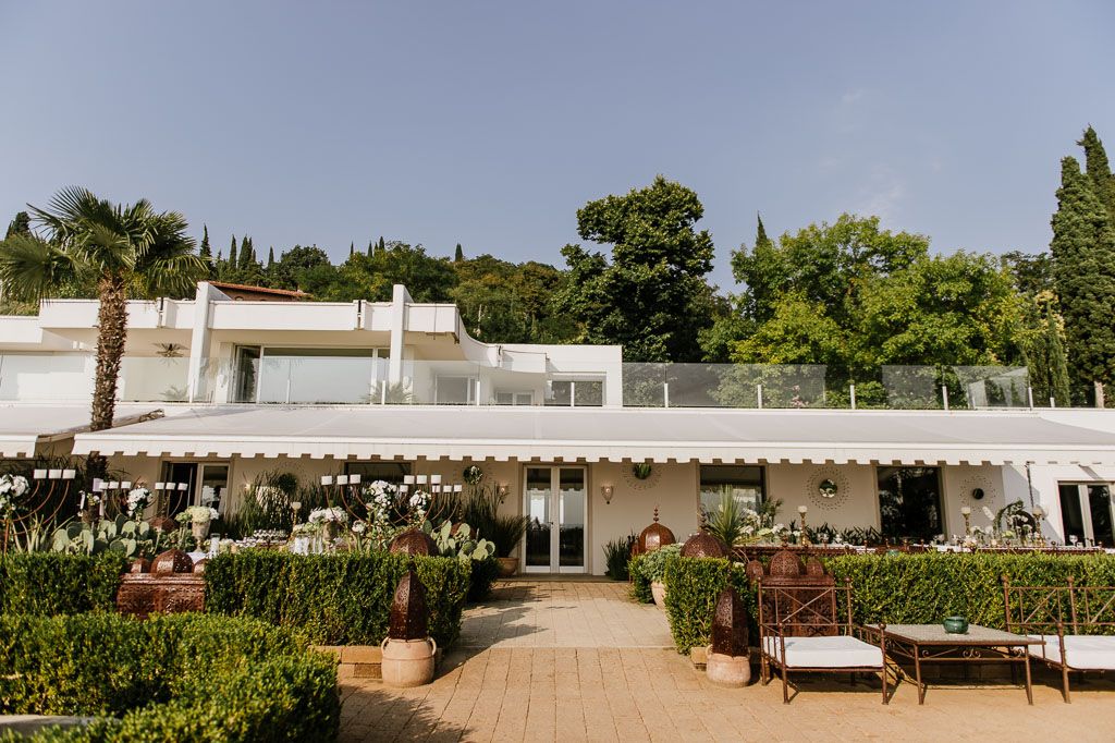 Mediterranean wedding venue with tall cypress trees and white decor under a bright sunny sky.