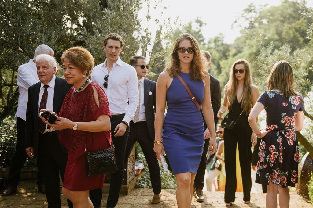 Wedding guests mingle outdoors during a sunny garden celebration.