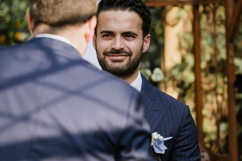 Wedding party stands together outdoors under trees in formal attire.