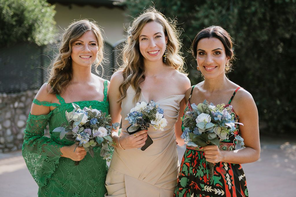 Wedding party members in green dresses and summer attire pose together outdoors.