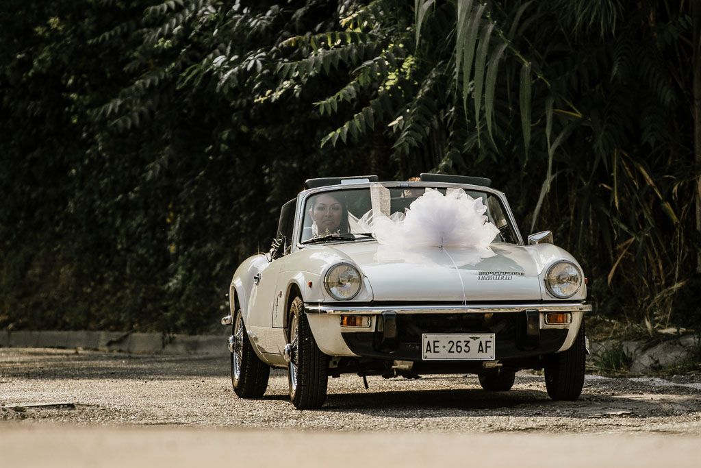 Classic white vintage car parked amongst trees in outdoor setting.