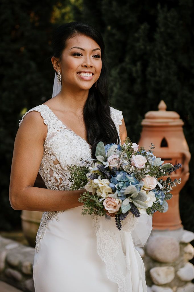 A bride in a lace wedding gown holds a beautiful bouquet of blue and cream flowers.