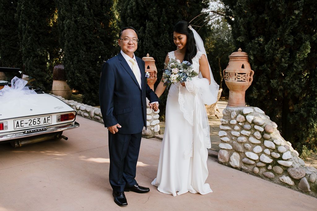 Elegant wedding portrait where newlyweds walk together along a stone-lined path through garden landscaping.