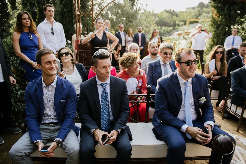 Wedding guests seated in rows outdoors surrounded by natural greenery and trees.