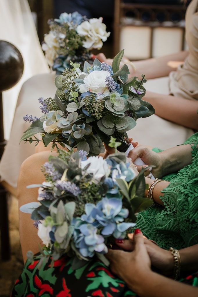 Close up of wedding bouquets with blue hydrangeas, white roses and eucalyptus leaves being held.