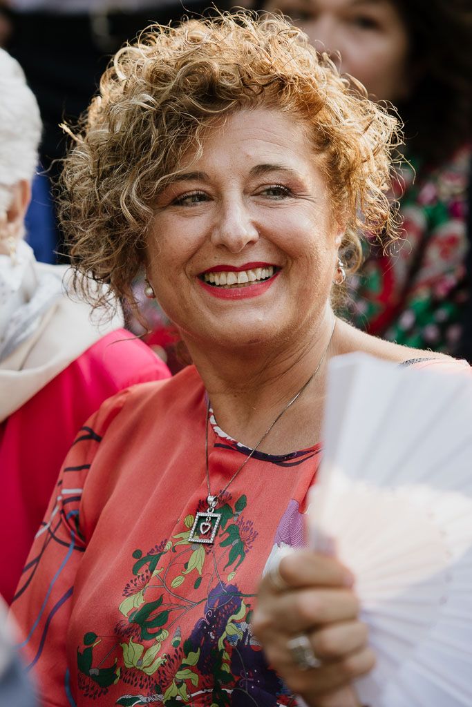 Wedding guest wearing a coral-colored floral dress smiles warmly during the celebration.