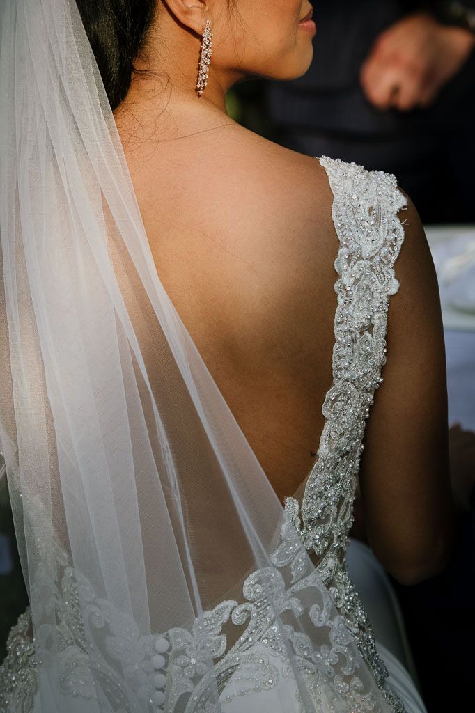 Close-up detail of intricate lace beading on back of white wedding dress with sheer veil.
