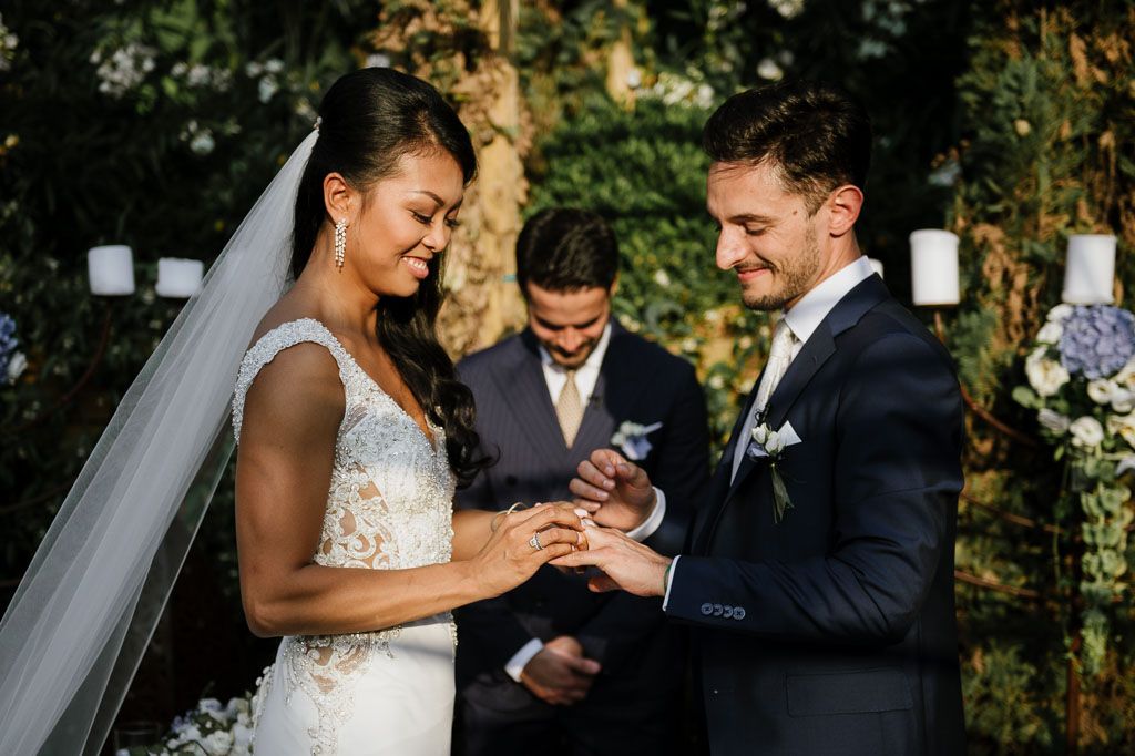 Wedding couple shares playful moment while exchanging rings during outdoor garden ceremony.