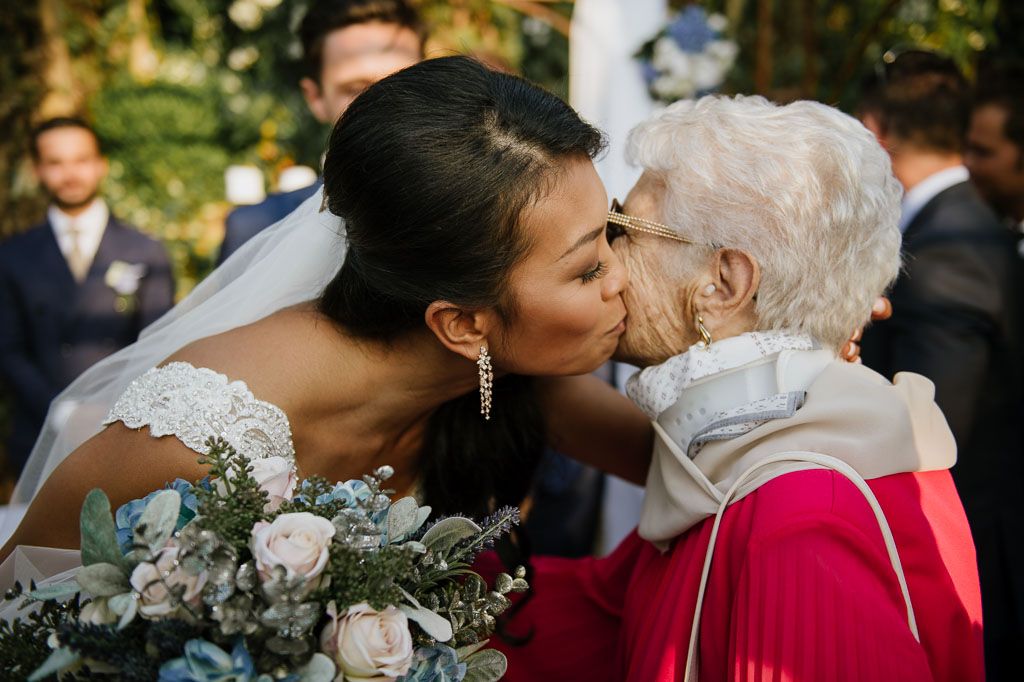 A touching moment between a bride in white and an elderly guest in pink at a wedding celebration.