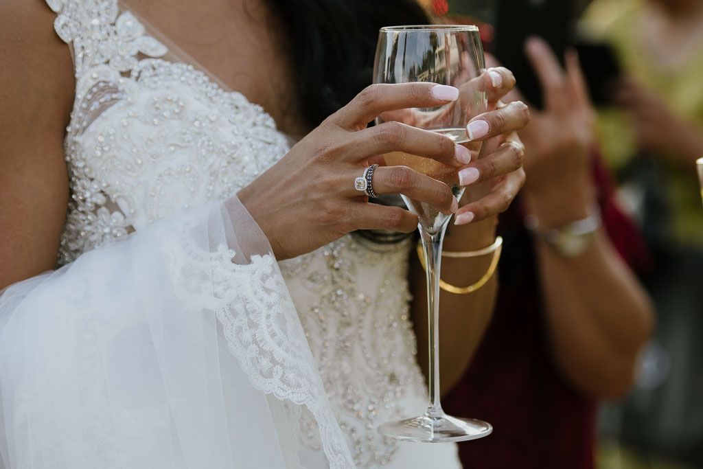 Close-up shot of a bride in lace holding a champagne glass showing her wedding ring.