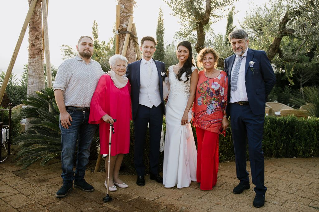 Wedding party poses together outdoors against a backdrop of trees.