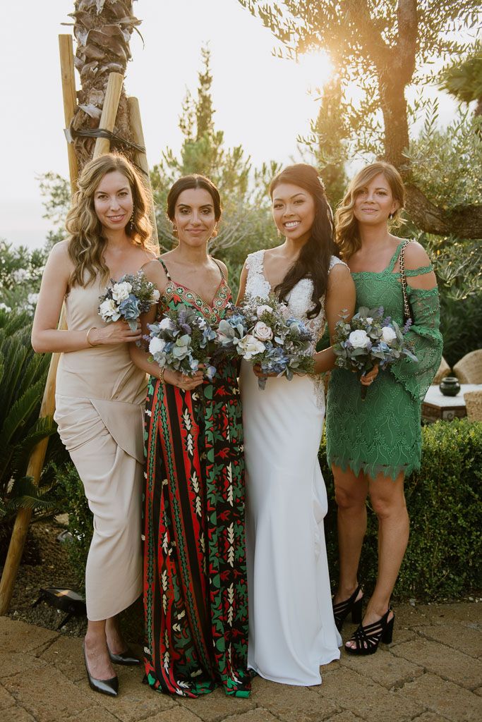 Wedding party poses together in mix of green and floral dresses holding bouquets at sunset.