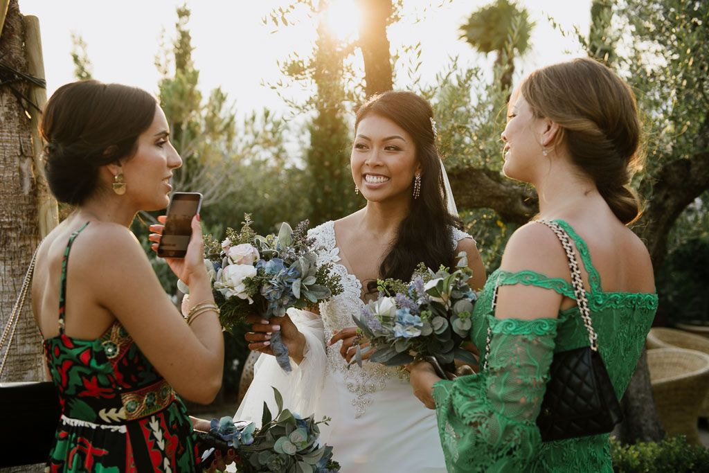 Bride in white dress chatting with guests in colorful attire during sunset reception.