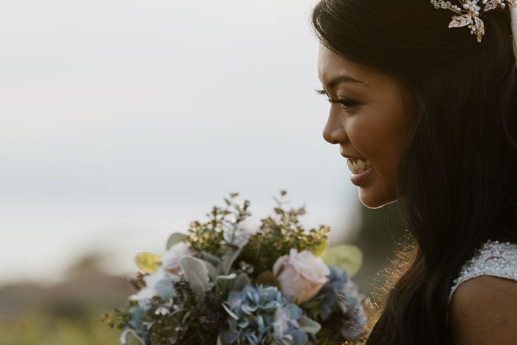 Side profile view of someone holding a pastel bouquet with delicate flowers against a soft sky.
