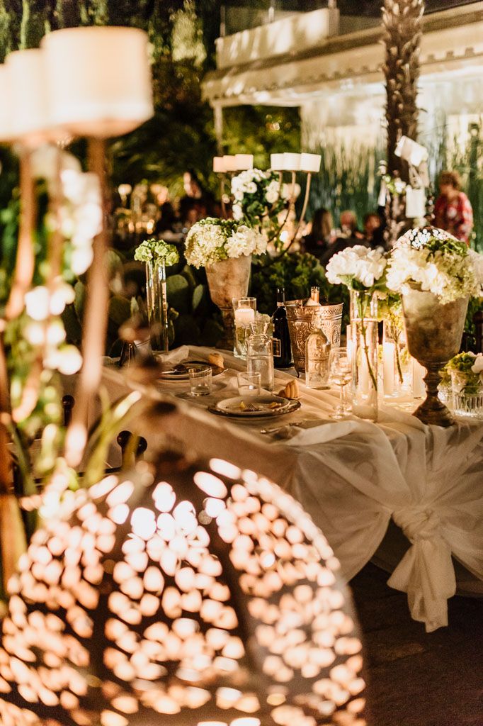 Elegant wedding table setting with glowing lanterns and white hydrangea centerpieces in golden evening light.