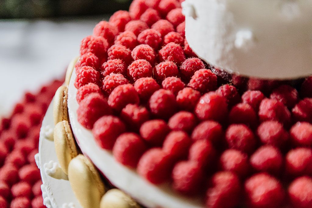 Close-up of a wedding cake decorated with vibrant red raspberries in a precise pattern.