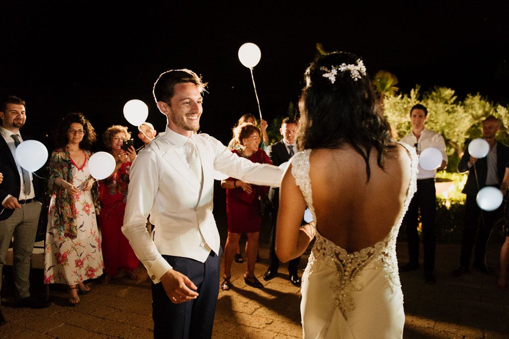 Wedding party dances under glowing white lanterns during an outdoor evening celebration.
