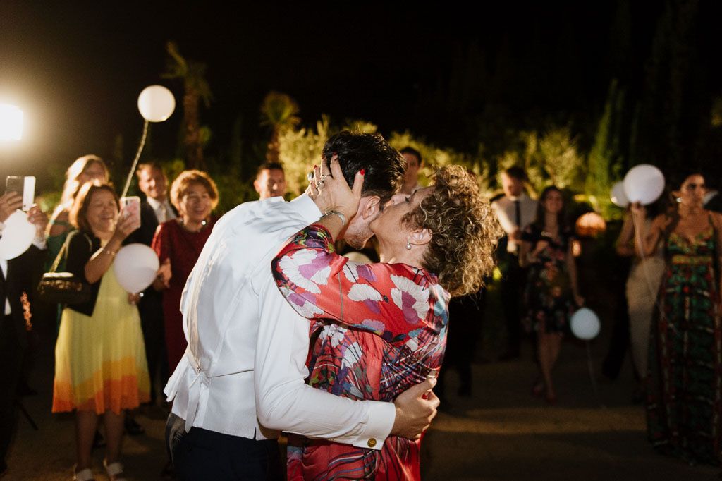 People dancing outdoors at a nighttime celebration illuminated by string lights and festive lighting.