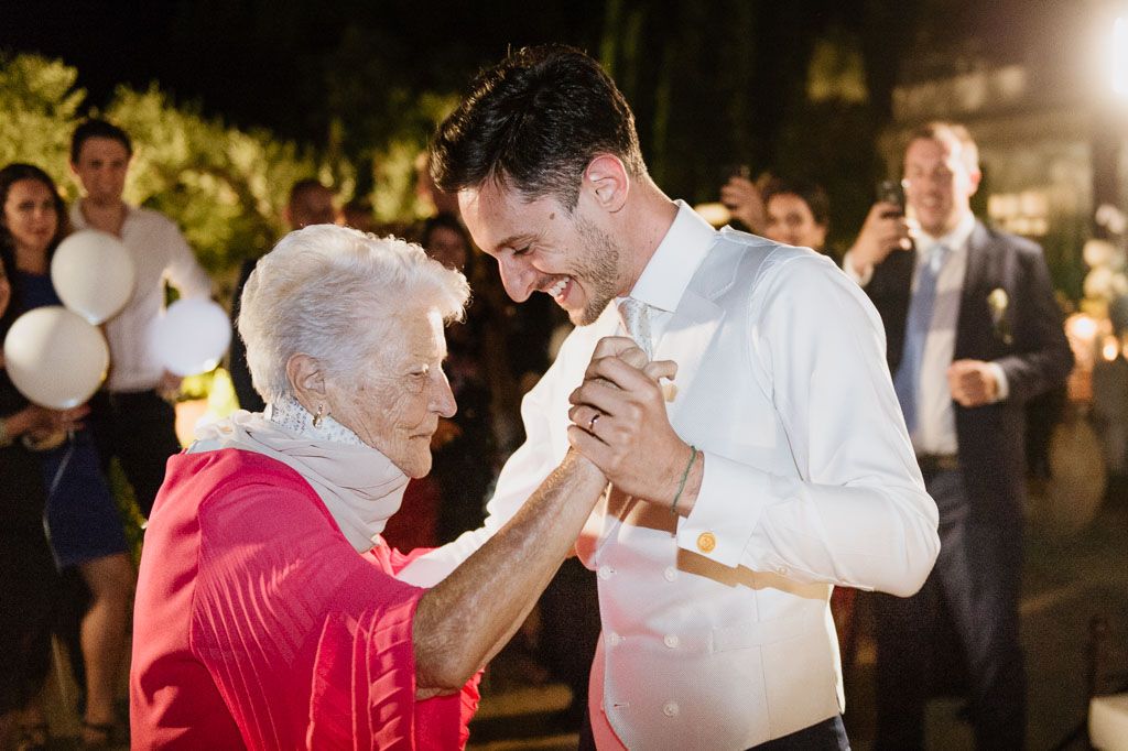 Wedding guests dance together beneath glowing lights at an elegant evening reception celebration.