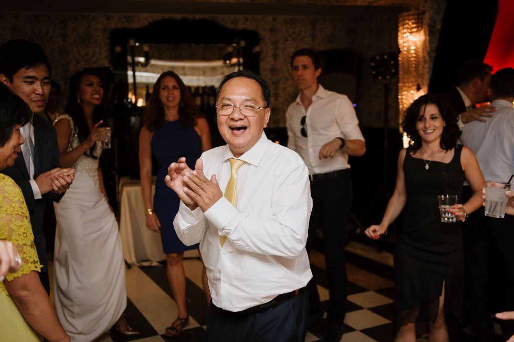 Wedding guests enjoying themselves on the dance floor at a reception with people clapping and dancing.