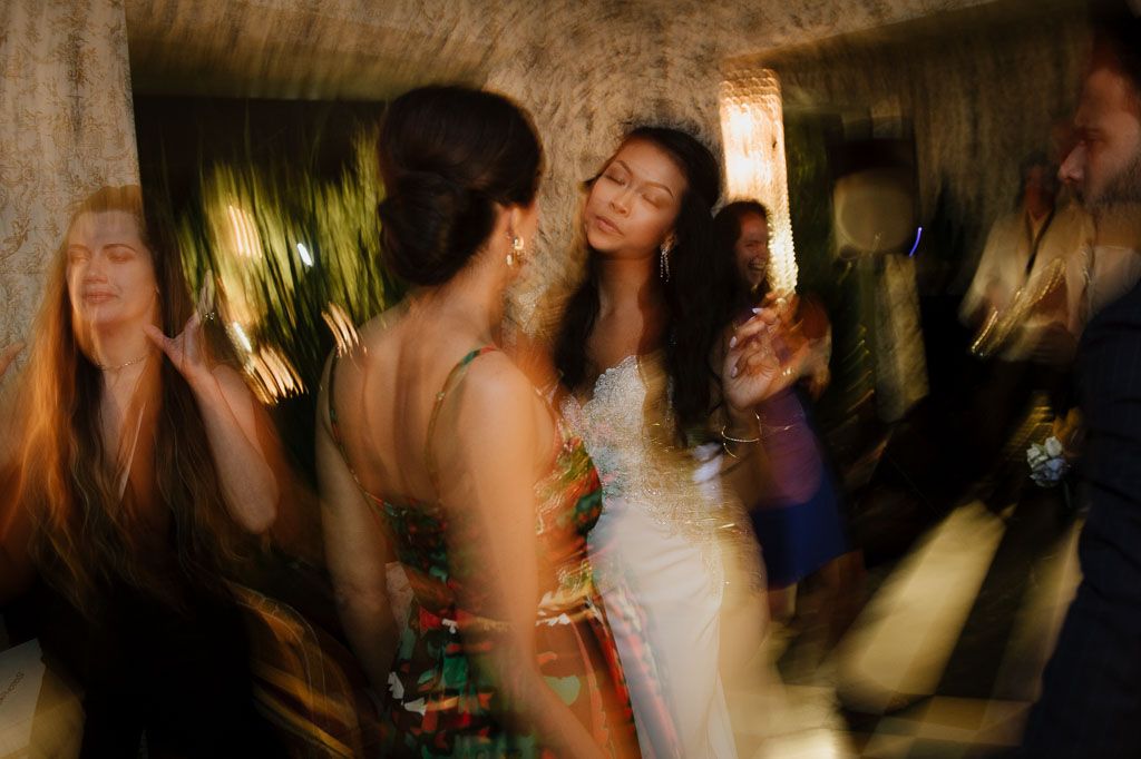 Blurred motion shot of wedding guests dancing and celebrating at a dimly lit reception venue.