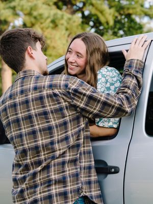 A couple sharing a sweet moment through a car window in a sunny outdoor setting.
