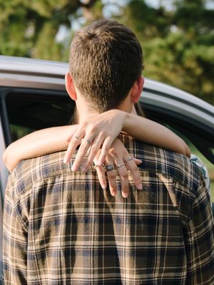 Close-up of hands with rings embracing around a plaid shirt, showing an intimate moment.