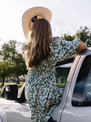 A scenic countryside photo series featuring someone in a floral dress leaning against a parked vehicle.