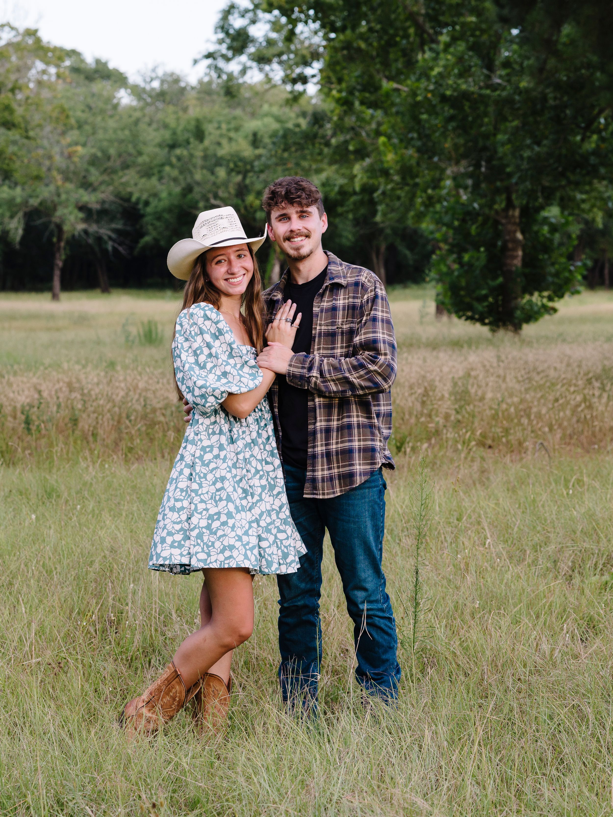 Romantic couple shares tender moments together in a sunny meadow with tall grass and trees.