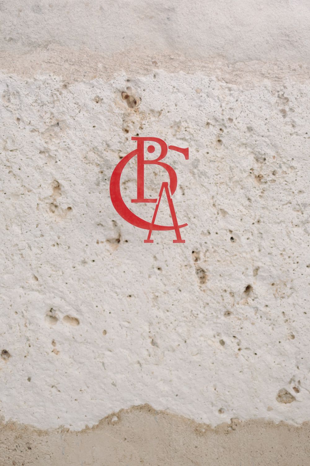 A red monogram logo combining the letters C, P, and A painted on a textured white stone or concrete surface.