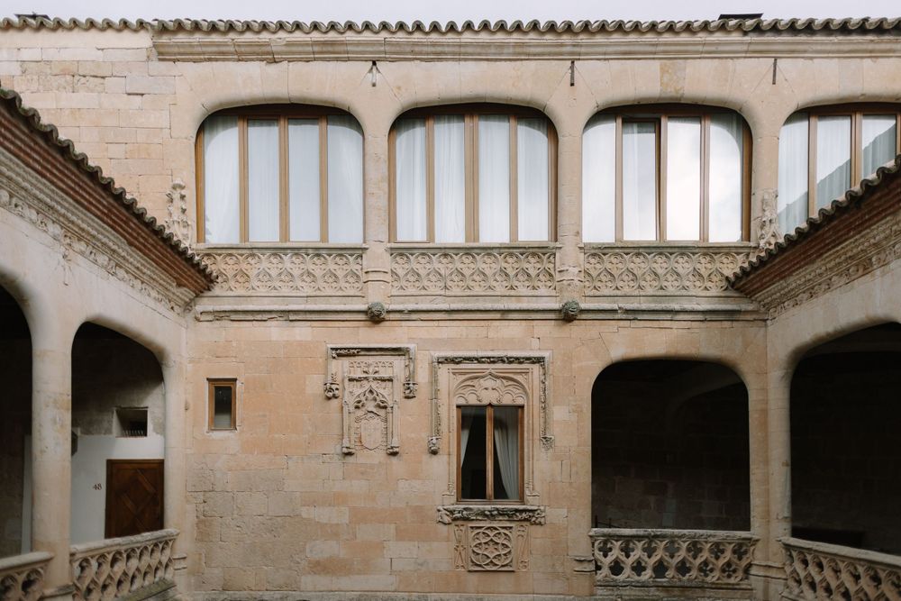 Architectural detail of a historic Spanish courtyard with arched windows and ornate stone carvings in beige limestone.