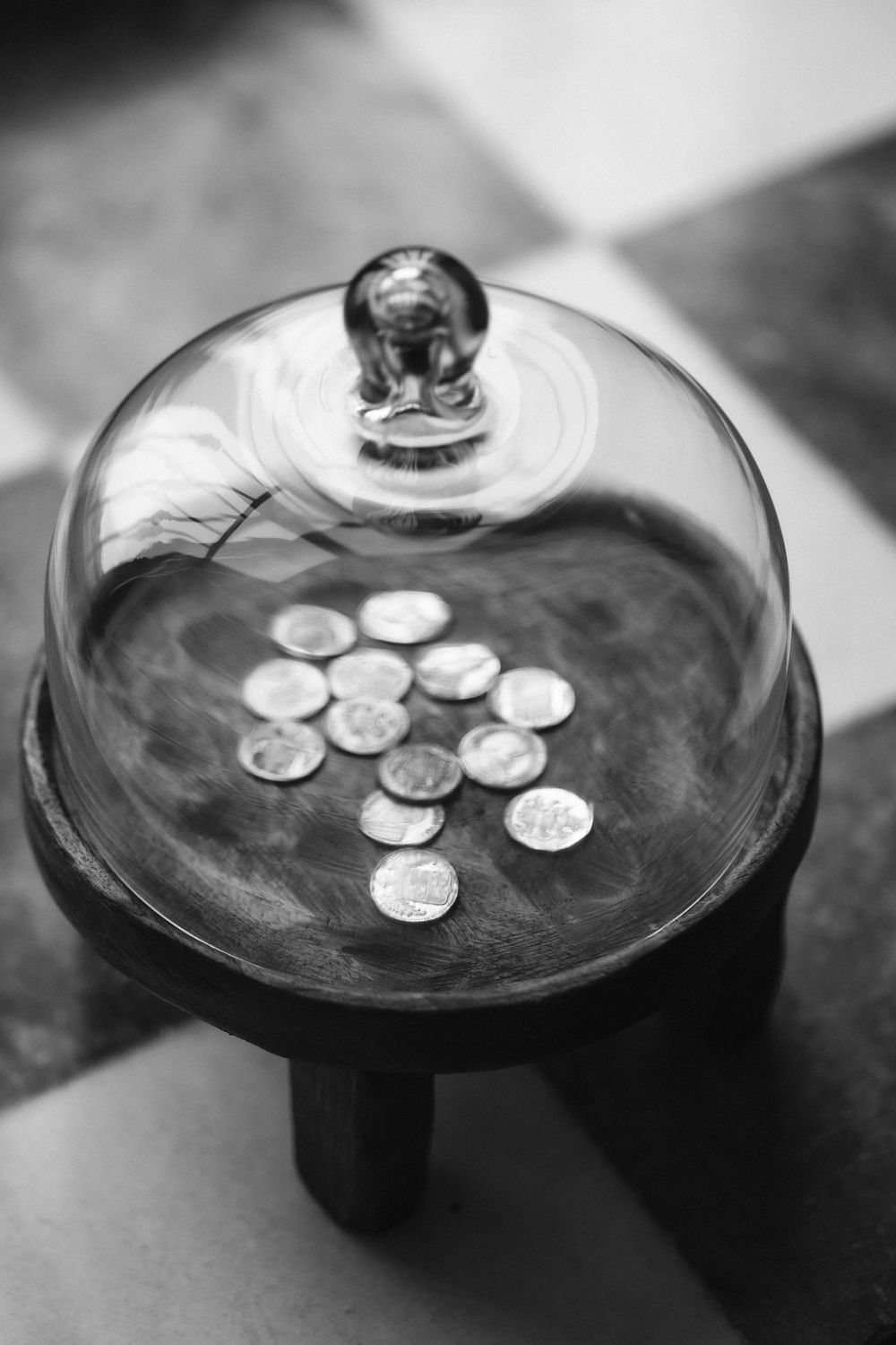 Several silver coins arranged in a dollar sign pattern under a glass dome cloche on a dark display stand.
