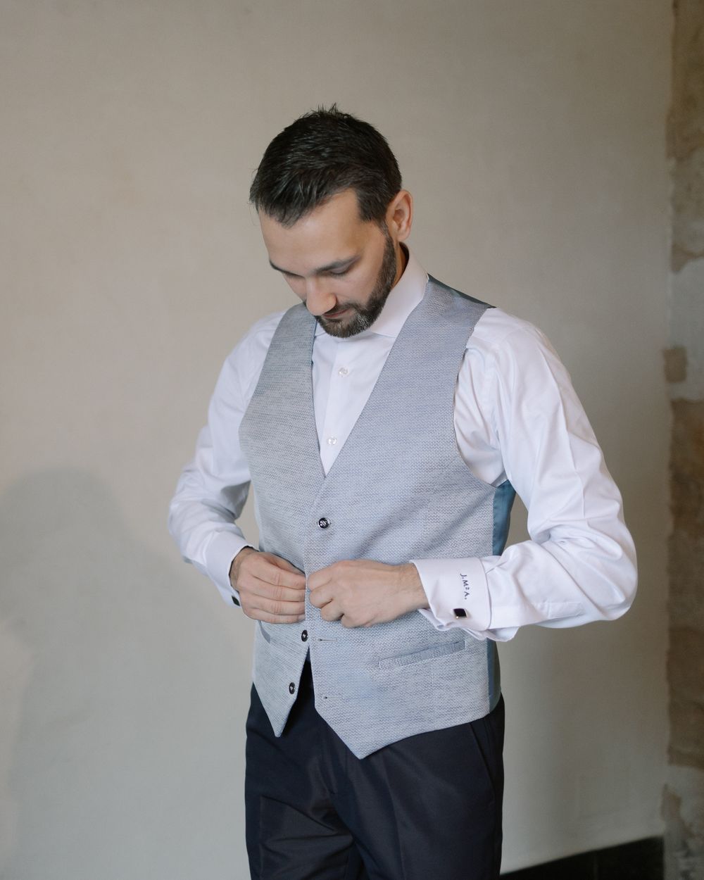 Someone buttons up a light gray vest over a crisp white dress shirt while getting dressed formally.