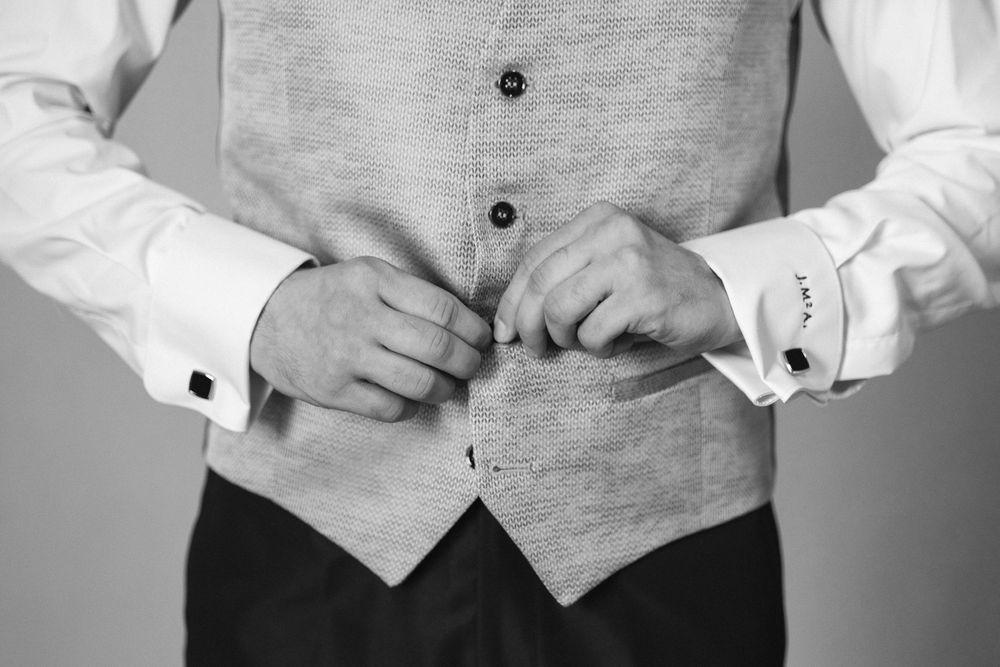 Close-up of someone buttoning a light gray vest over a white dress shirt with cufflinks.