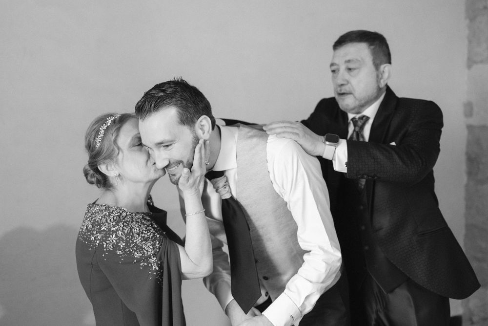 Three people interact in a playful black and white photo with someone whispering and another tapping on a shoulder.