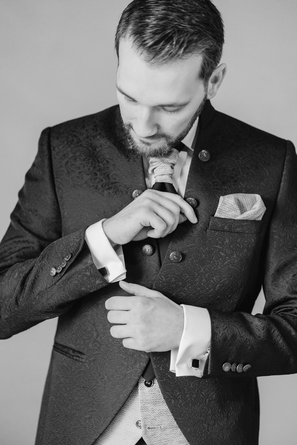 Black and white portrait of a well-dressed man in a formal suit and pocket square adjusting his cufflink.