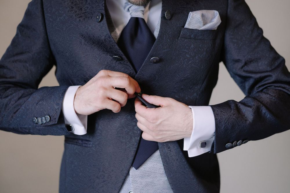 Close-up shot of someone adjusting a dark suit jacket with vest and light pocket square.