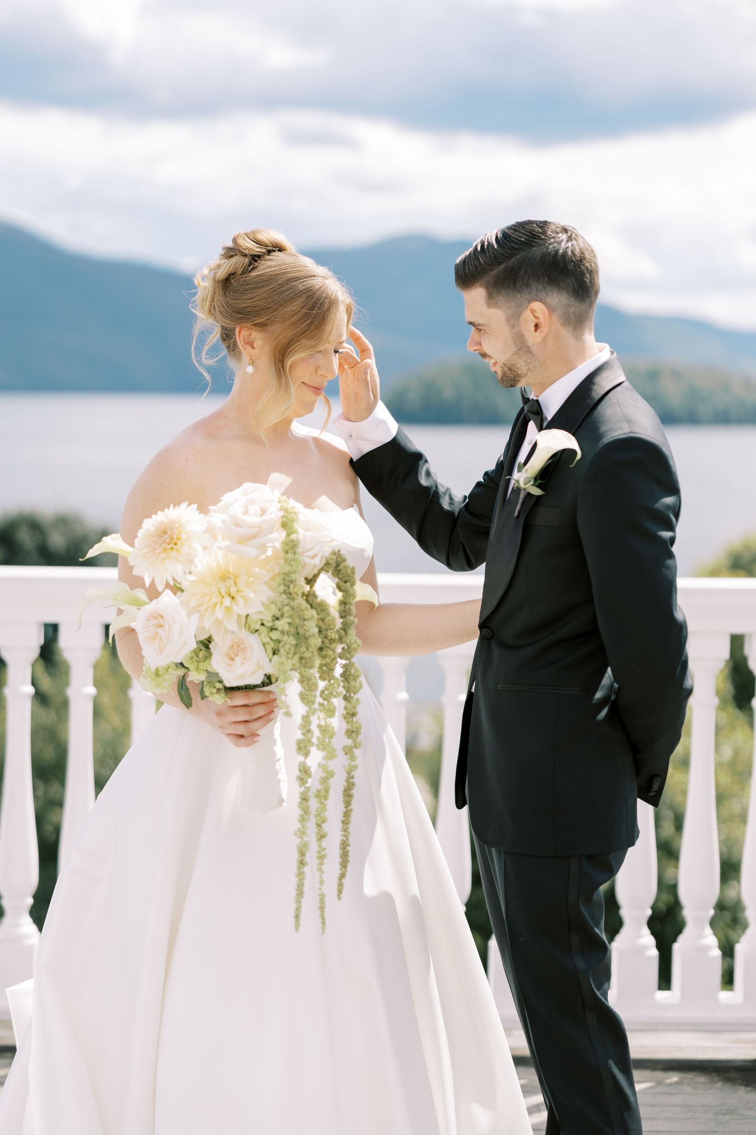 A couple shares a tender moment on a balcony overlooking a scenic mountain lake view.