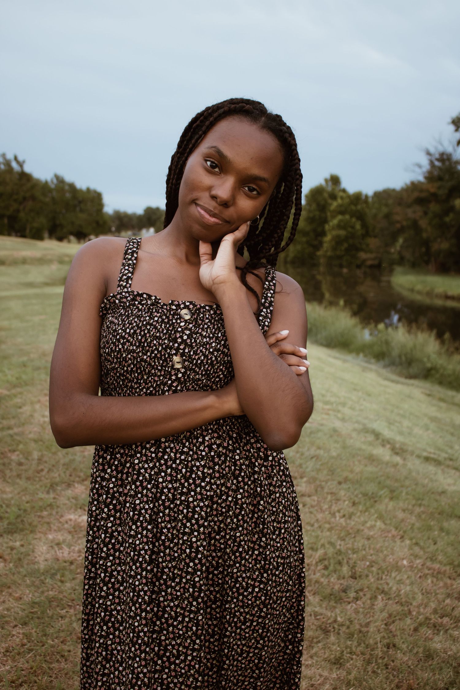 A person in a polka dot dress poses thoughtfully in a grassy field on a cloudy day.