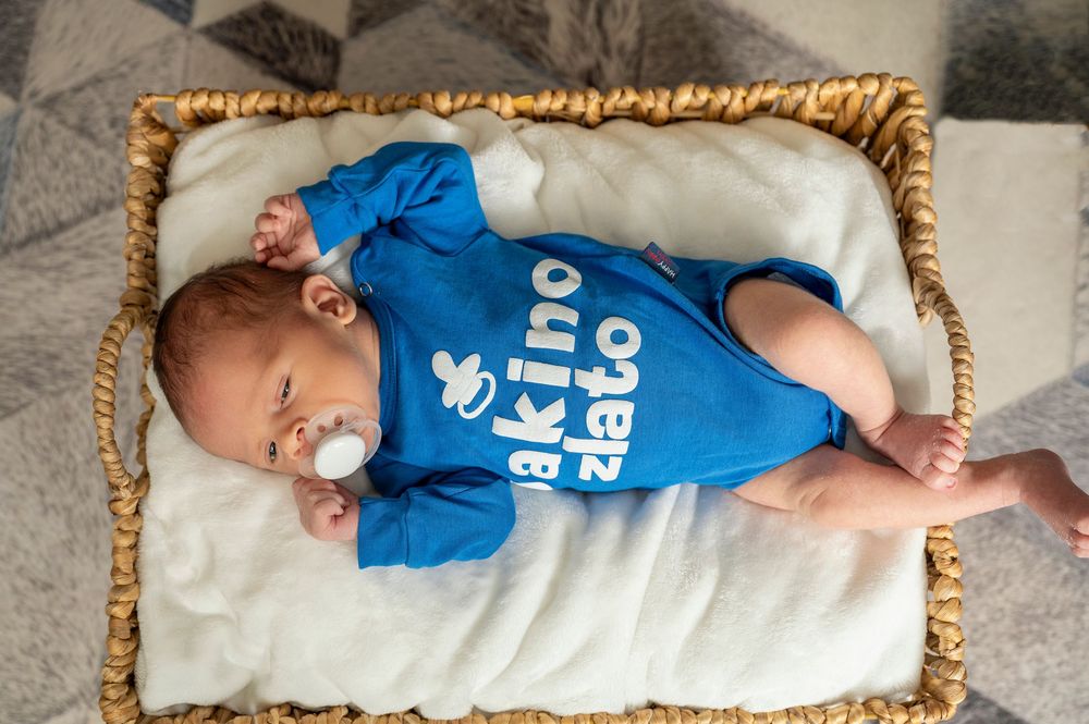 A sleeping baby wearing a blue onesie lies on a soft white cushion in a series of progressive shots.