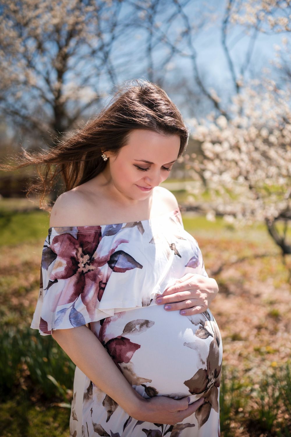 A person in a floral dress poses in a spring garden with blooming cherry blossoms in the background.