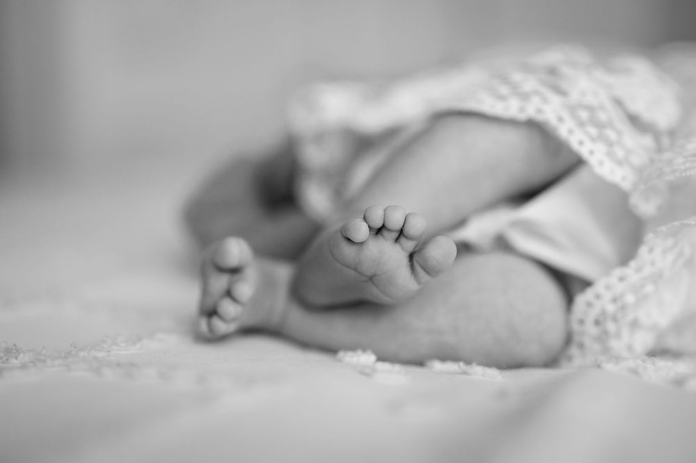 A black and white close-up photograph of tiny newborn baby feet wrapped in delicate lace.