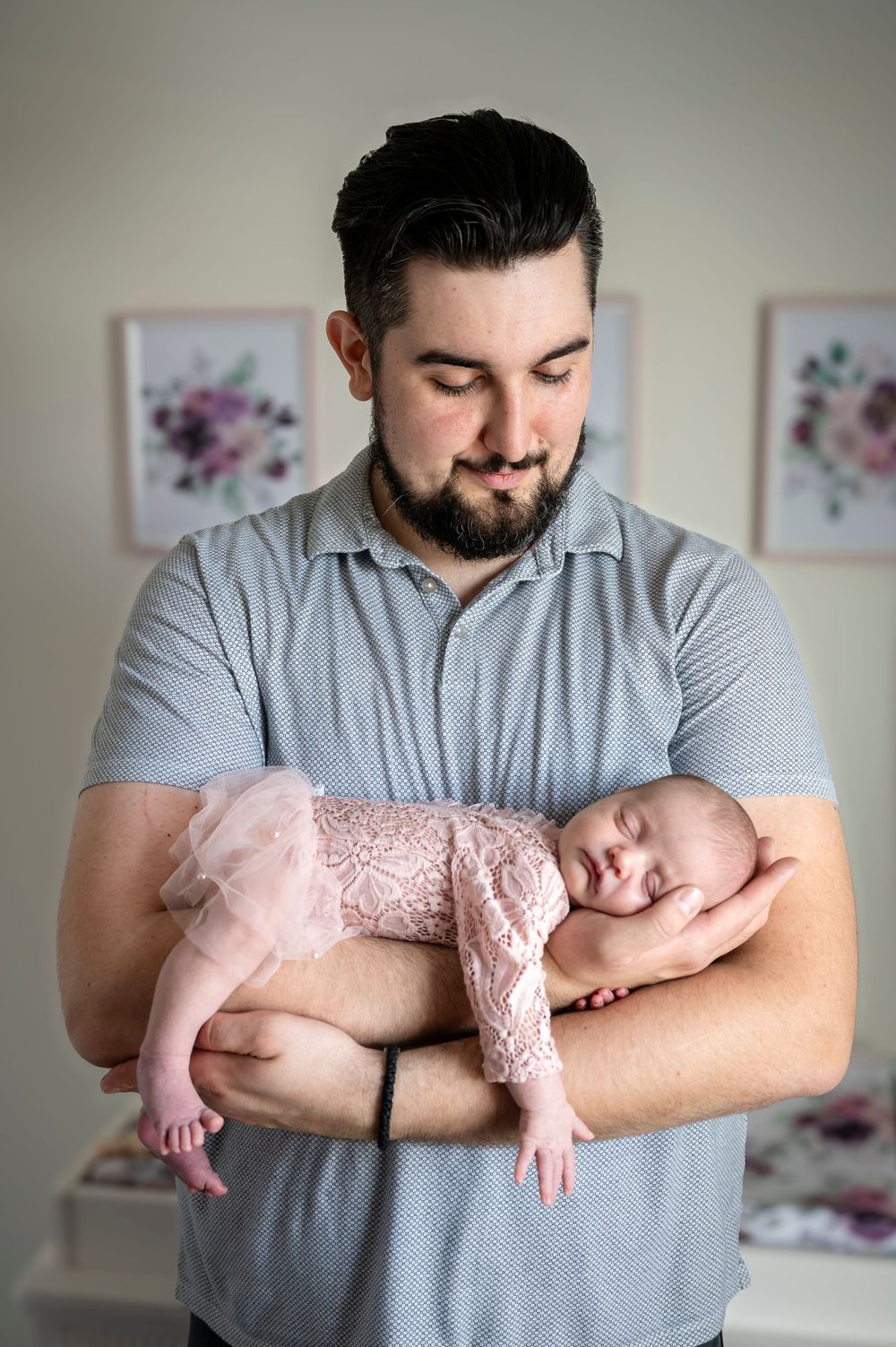 Baby in pink lace dress sleeping peacefully in father's arms wearing gray polo shirt.
