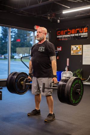 Strongman lifting heavy barbell during workout at Cerberus gym.