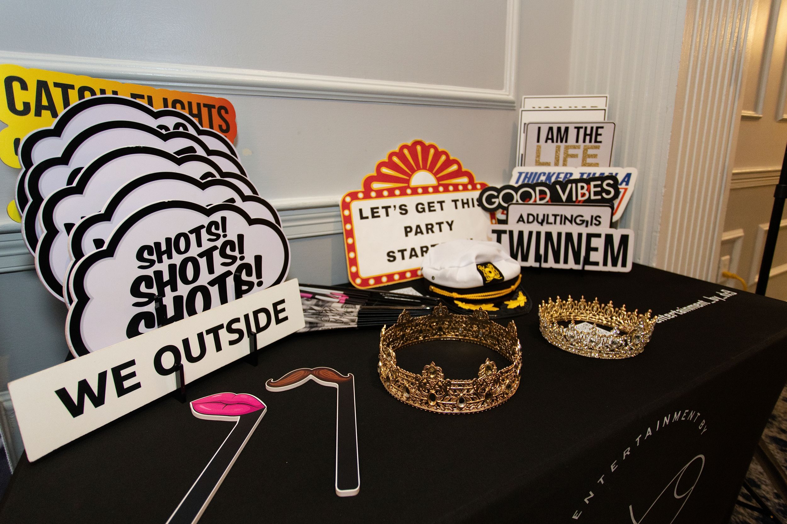 Event props and signs displayed on a black table including 'We Outside' and party-themed decorations.