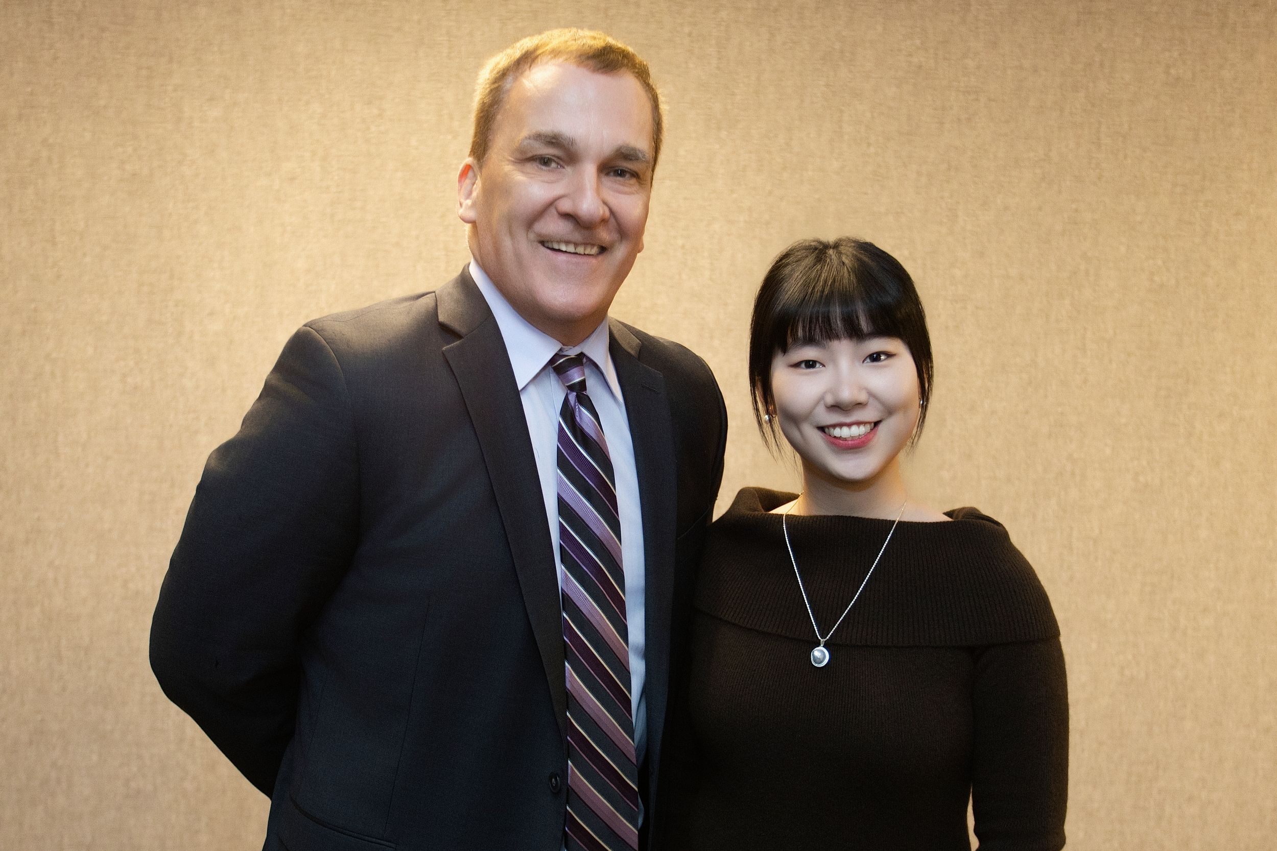 Professional headshots of two people in business attire against beige background.