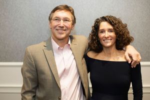Two people pose together at a formal event wearing business casual attire.