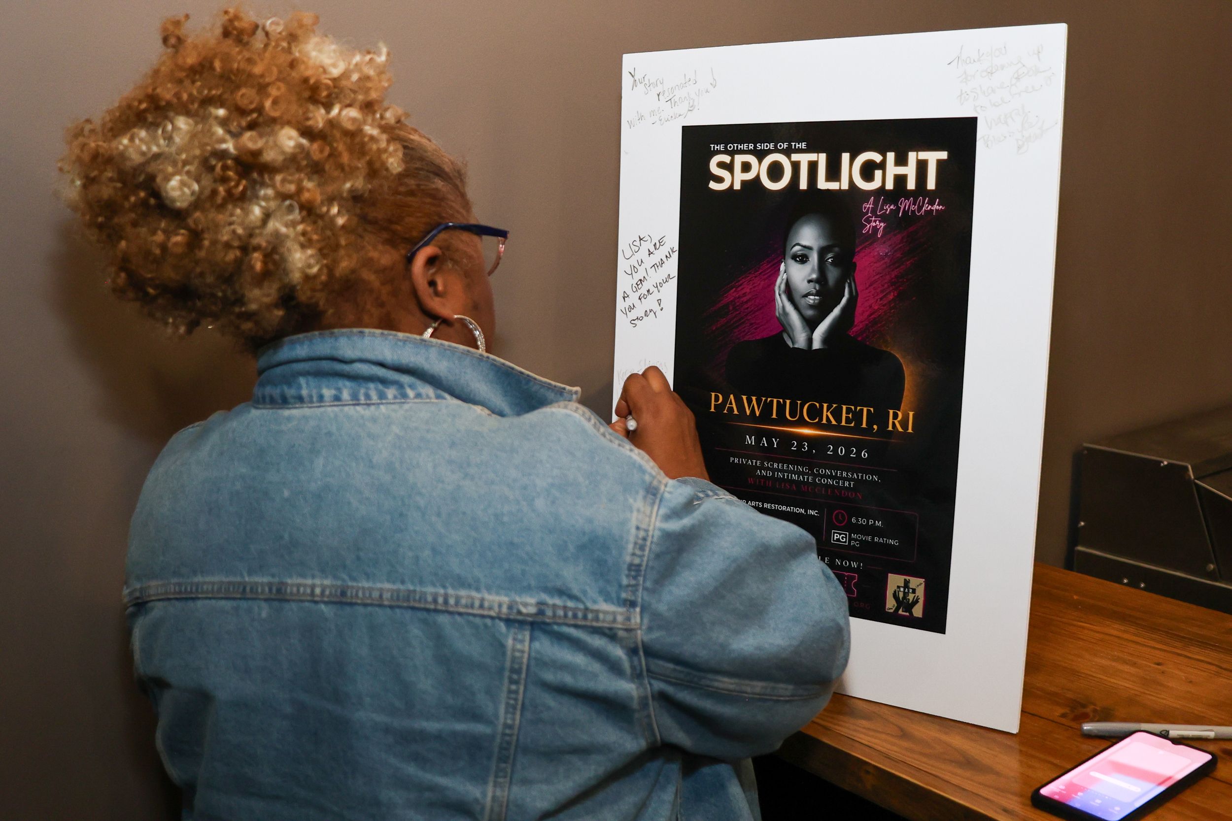 Person signing a Spotlight Pawtucket RI event poster mounted in a white frame on a wall.