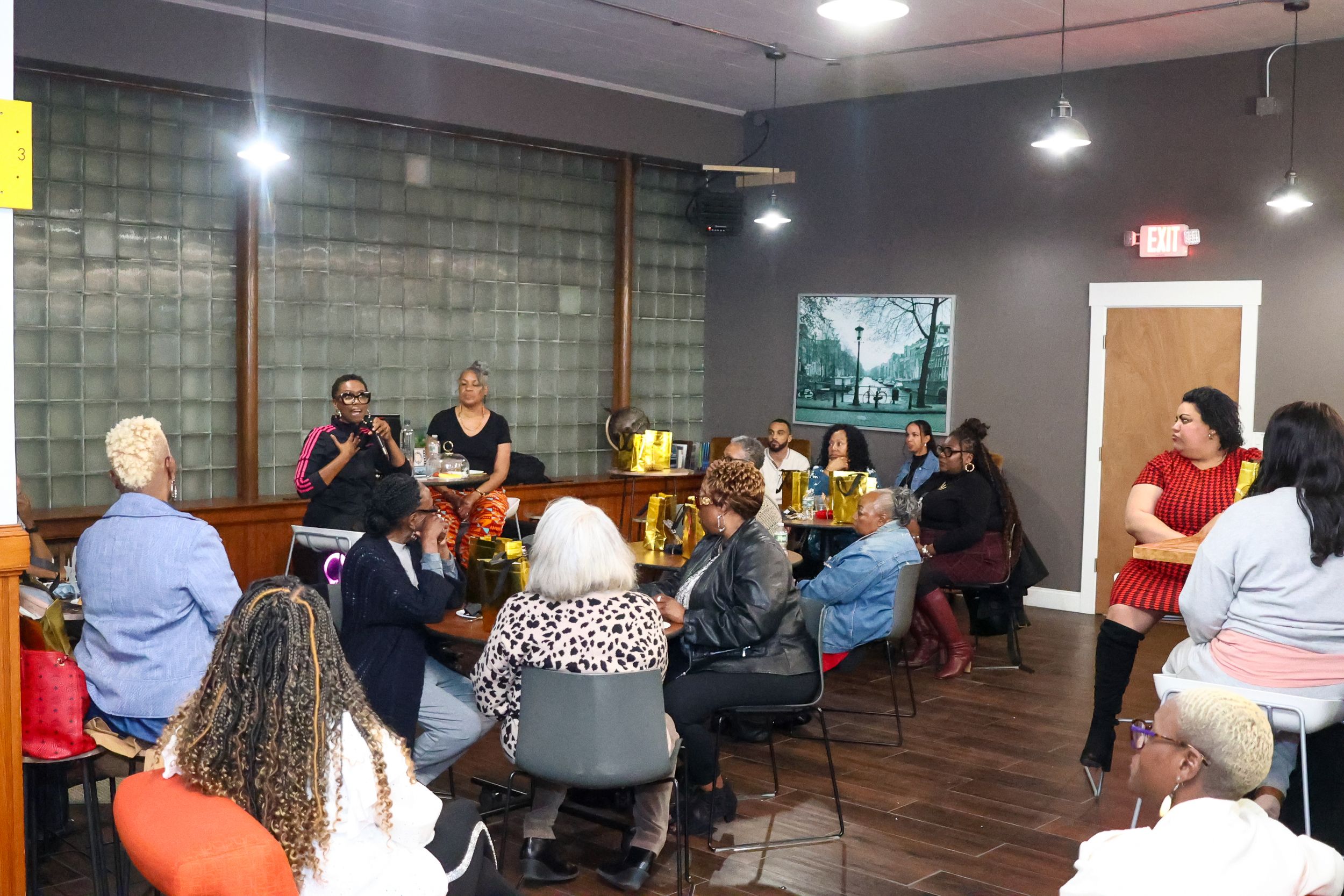 Diverse group of people gathered for a community meeting in a casual indoor space with gray walls.