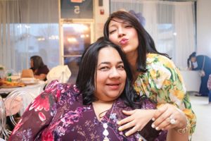Two friends in colorful floral outfits sharing a joyful moment at a casual indoor gathering.